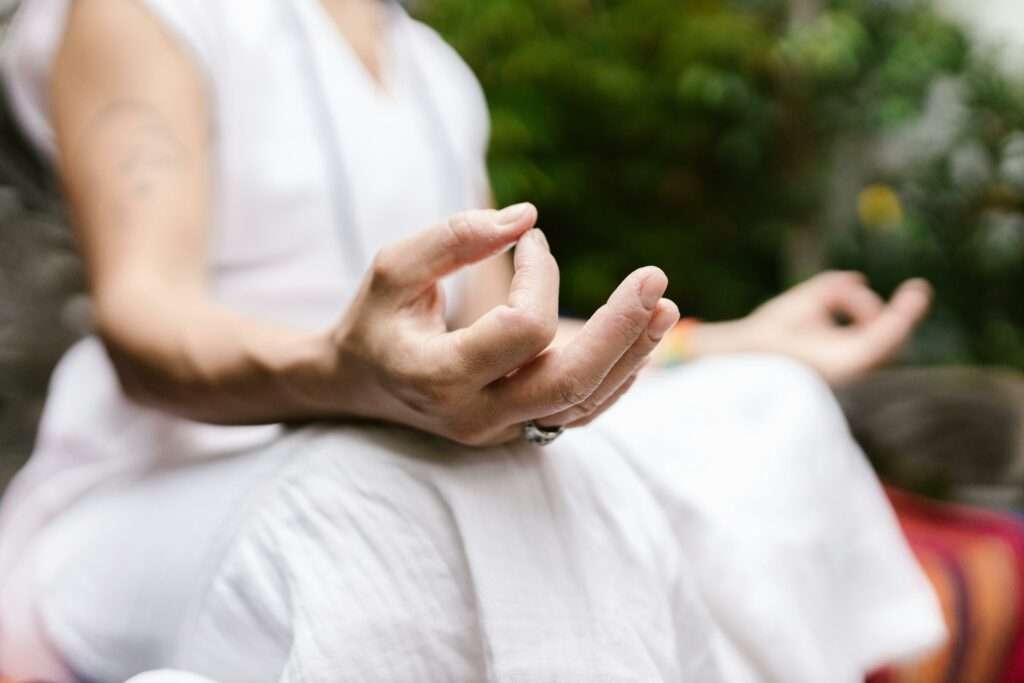 A person sits outdoors, focusing on their hands in a meditative mudra, embodying peace.